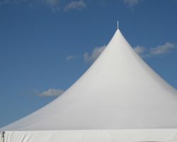 Photo of the peak of a large white tent with blue sky and clouds